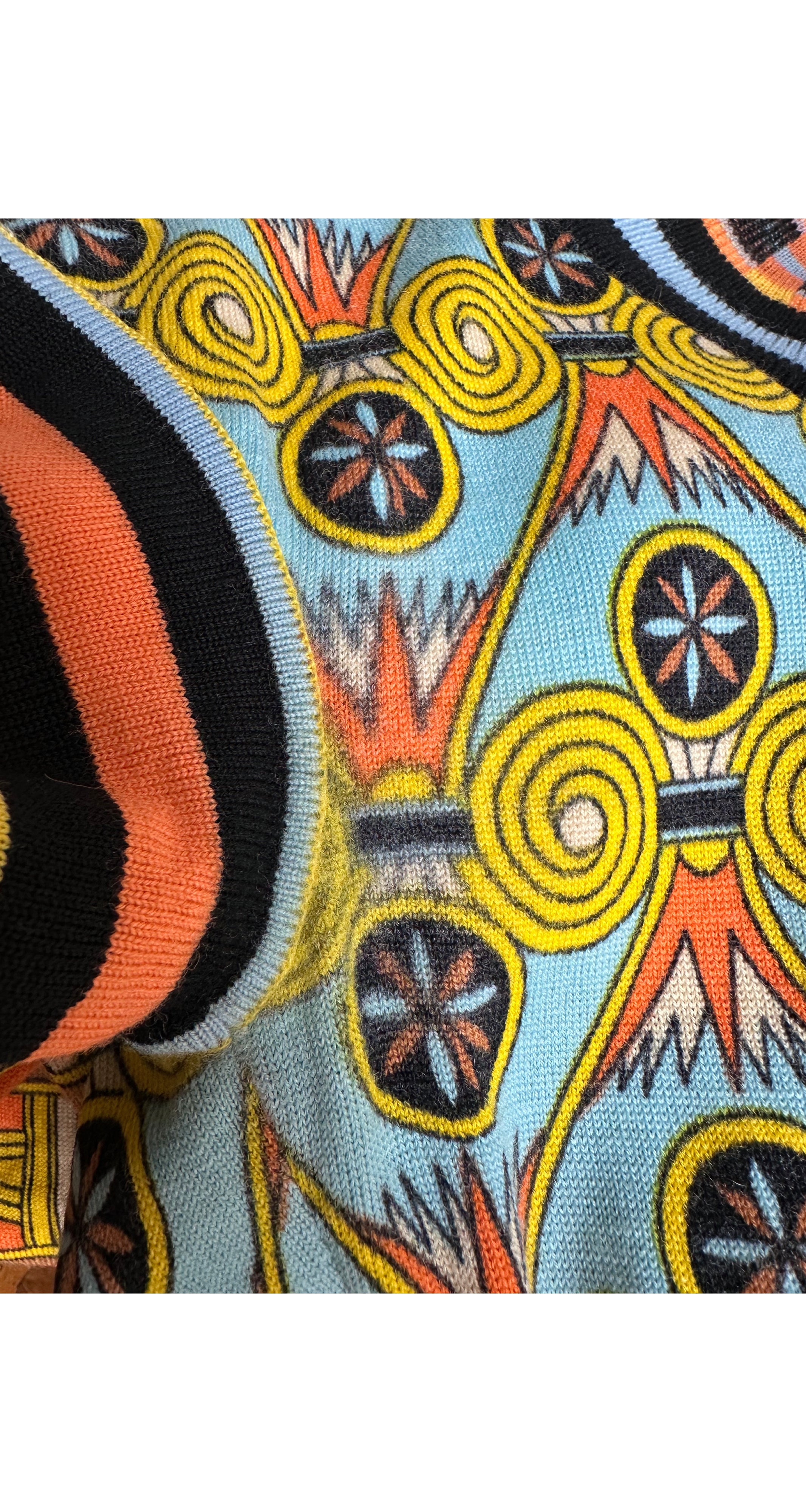 Close-up of a knit fabric with a colorful geometric pattern featuring yellow spirals, black and orange stripes, and a light blue background.