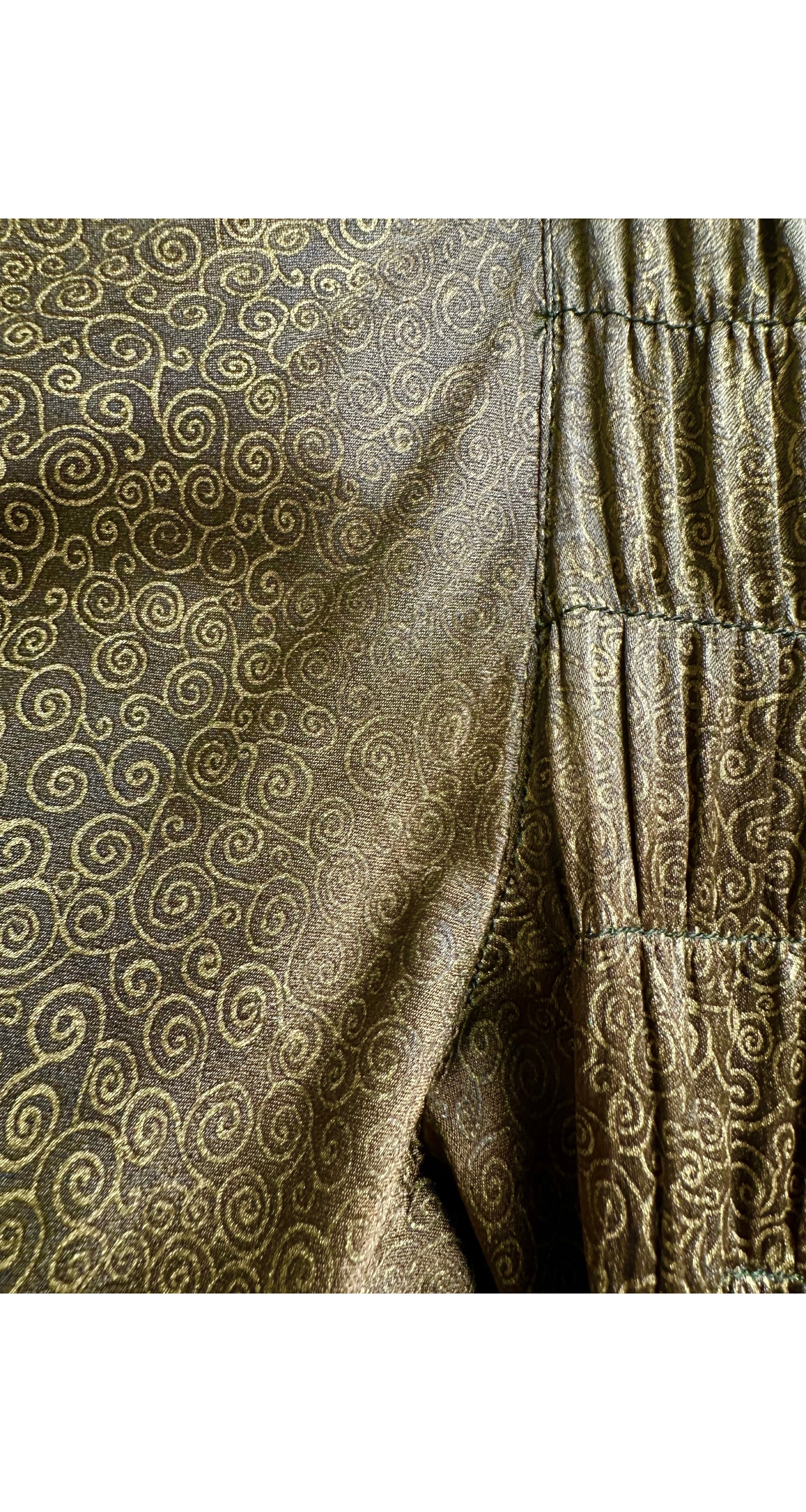 Close-up of a textured fabric with a metallic gold swirl pattern on a dark brown or bronze base, showing a gathered elastic seam.
