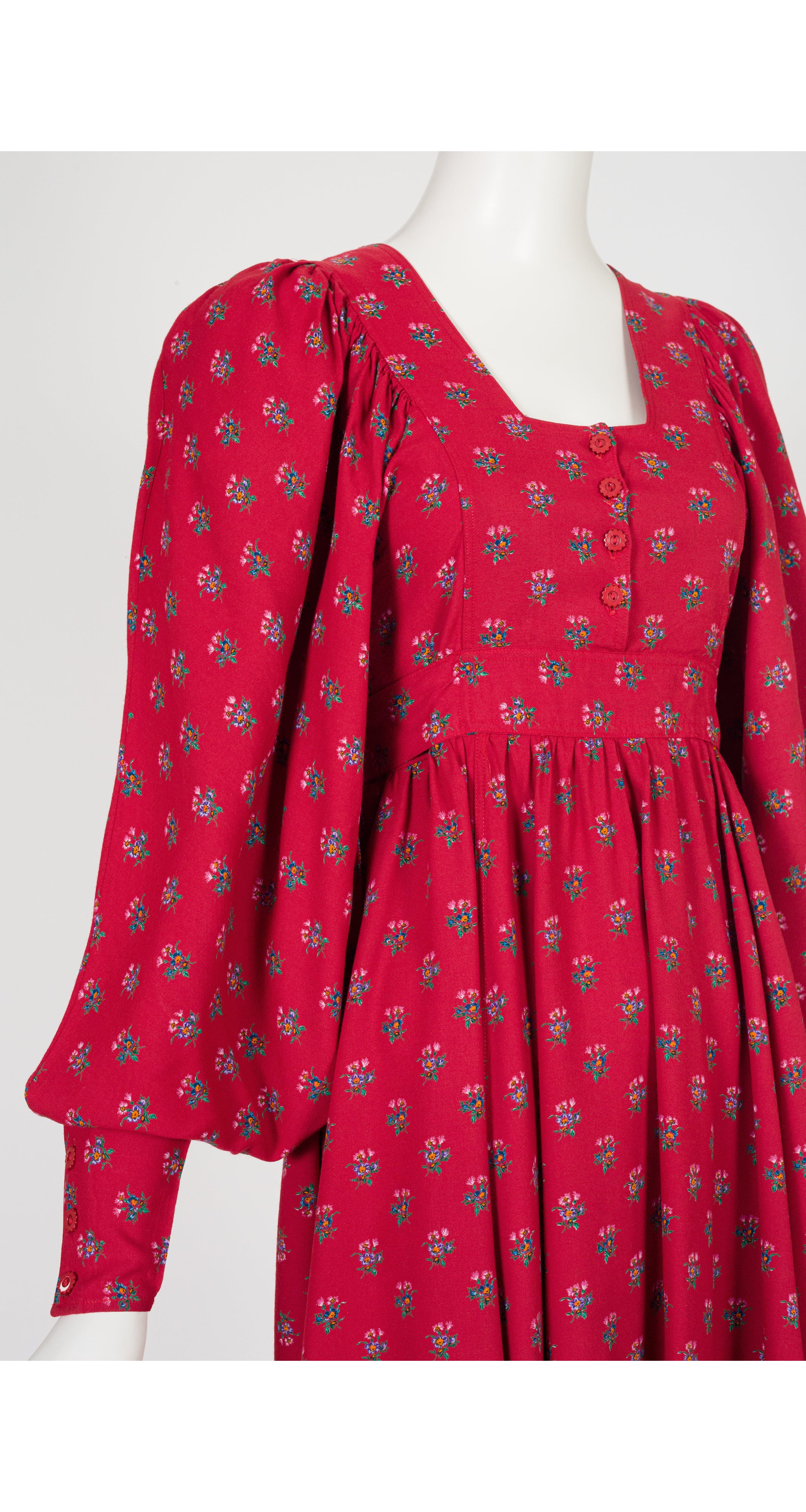 A 1970s Jeff Banks red long-sleeve dress with a small green and blue floral print, displayed on a white mannequin against a light gray background.