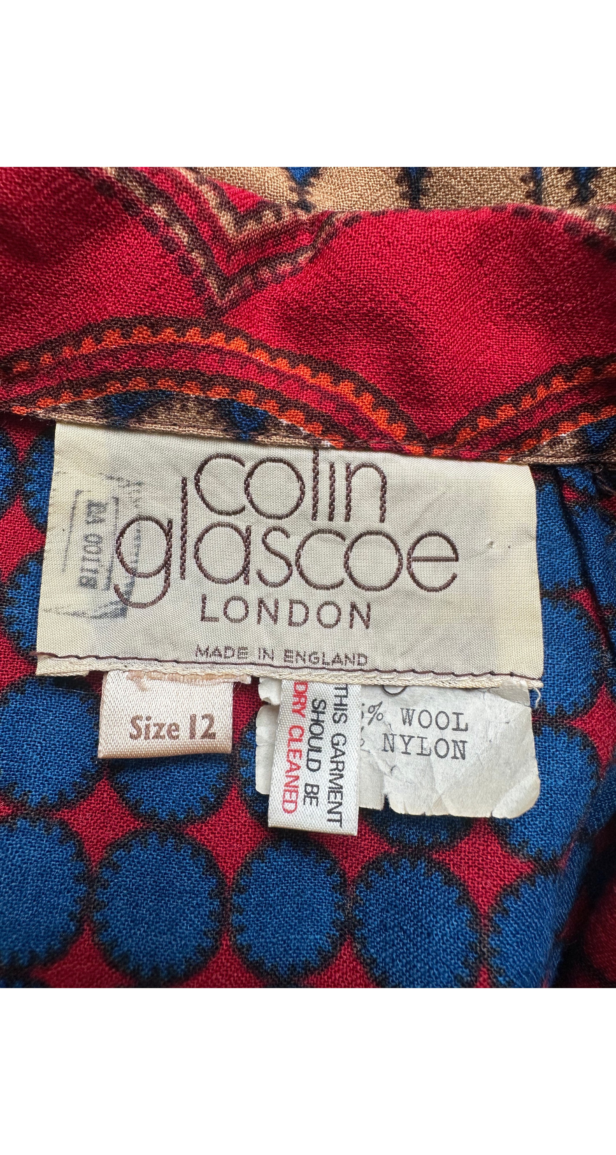 Close-up of a vintage Colin Glascoe London garment label on a red and blue patterned fabric background.