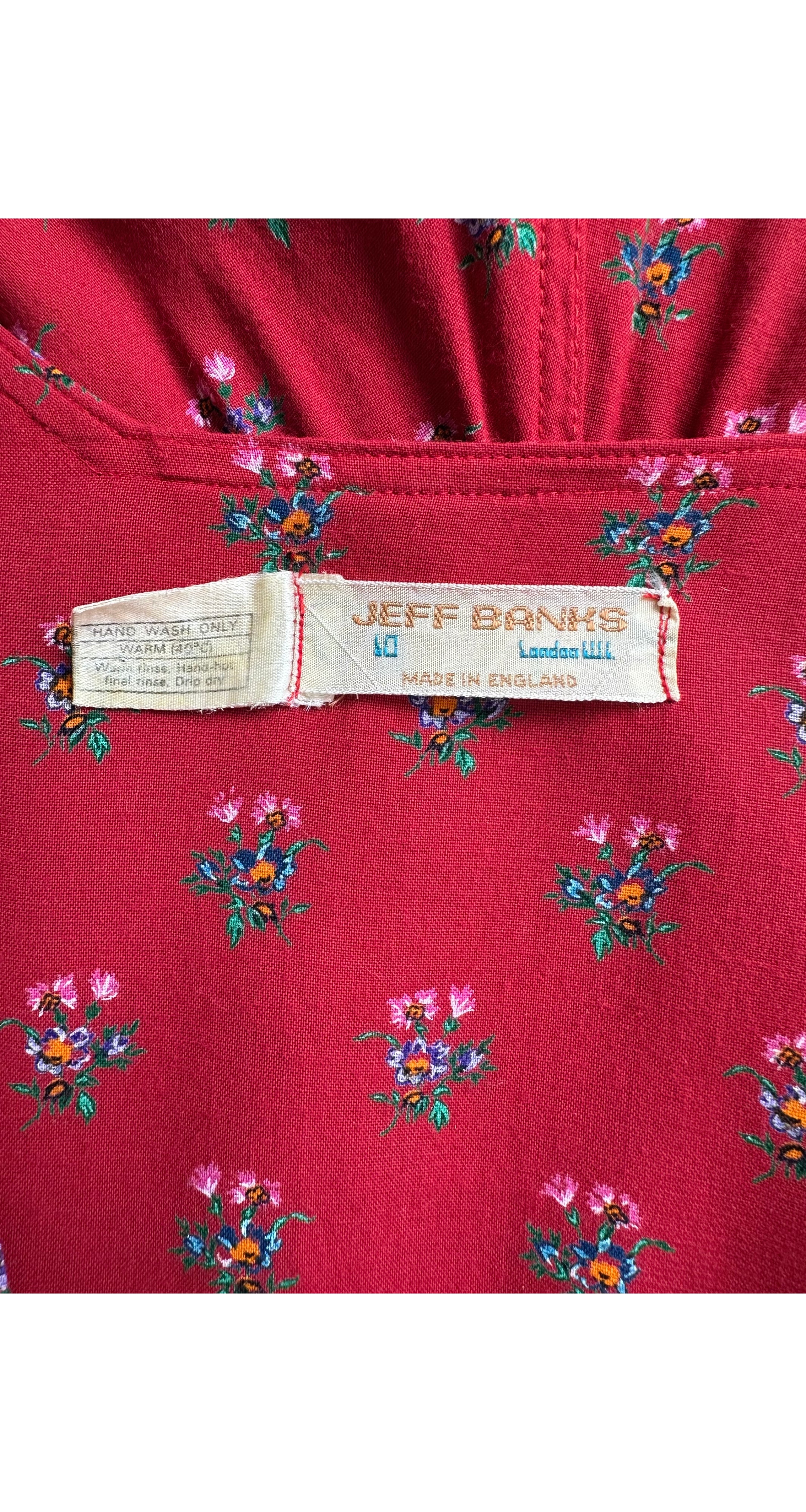 Close-up of a red fabric garment with a small multicolor floral print and a visible Jeff Banks London label.
