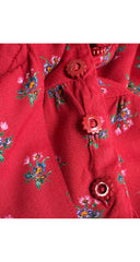 A close-up of a red fabric garment featuring a small-scale floral print in green, blue, and pink, detailed with matching red decorative buttons.