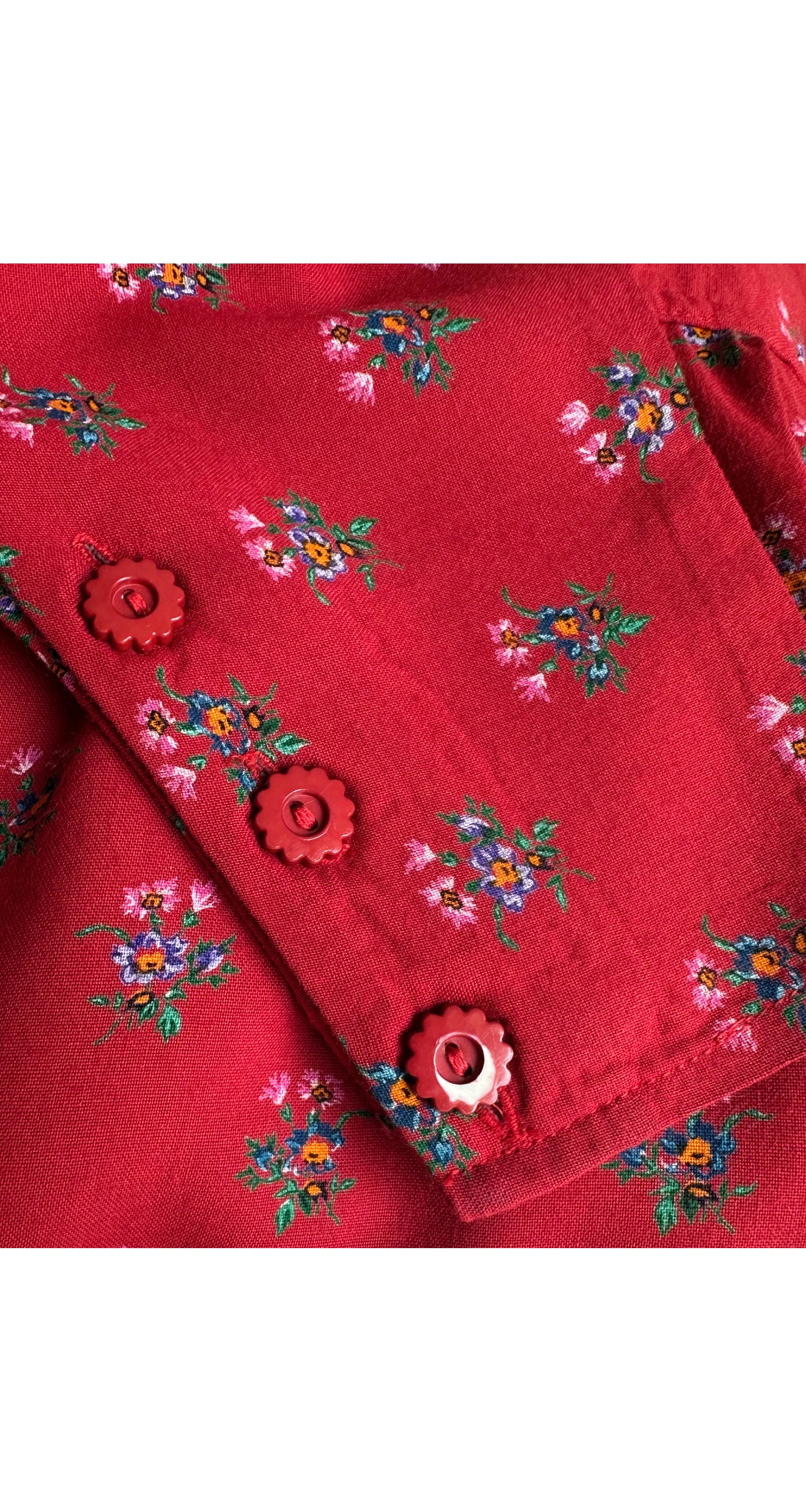 A close-up of a red fabric garment featuring a small multicolor floral pattern and decorative red buttons.