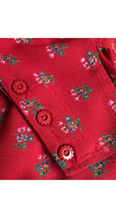 A close-up of a red fabric garment featuring a small multicolor floral pattern and decorative red buttons.