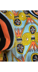 Close-up of a knit fabric with a colorful geometric pattern featuring yellow spirals, black and orange stripes, and a light blue background.