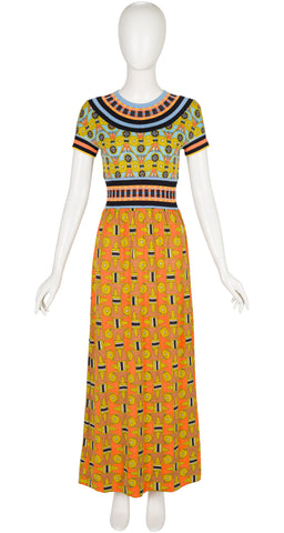 A 1970s Goldworm short-sleeve maxi dress with a colorful geometric and tribal-inspired print, displayed on a white mannequin against a plain white background.