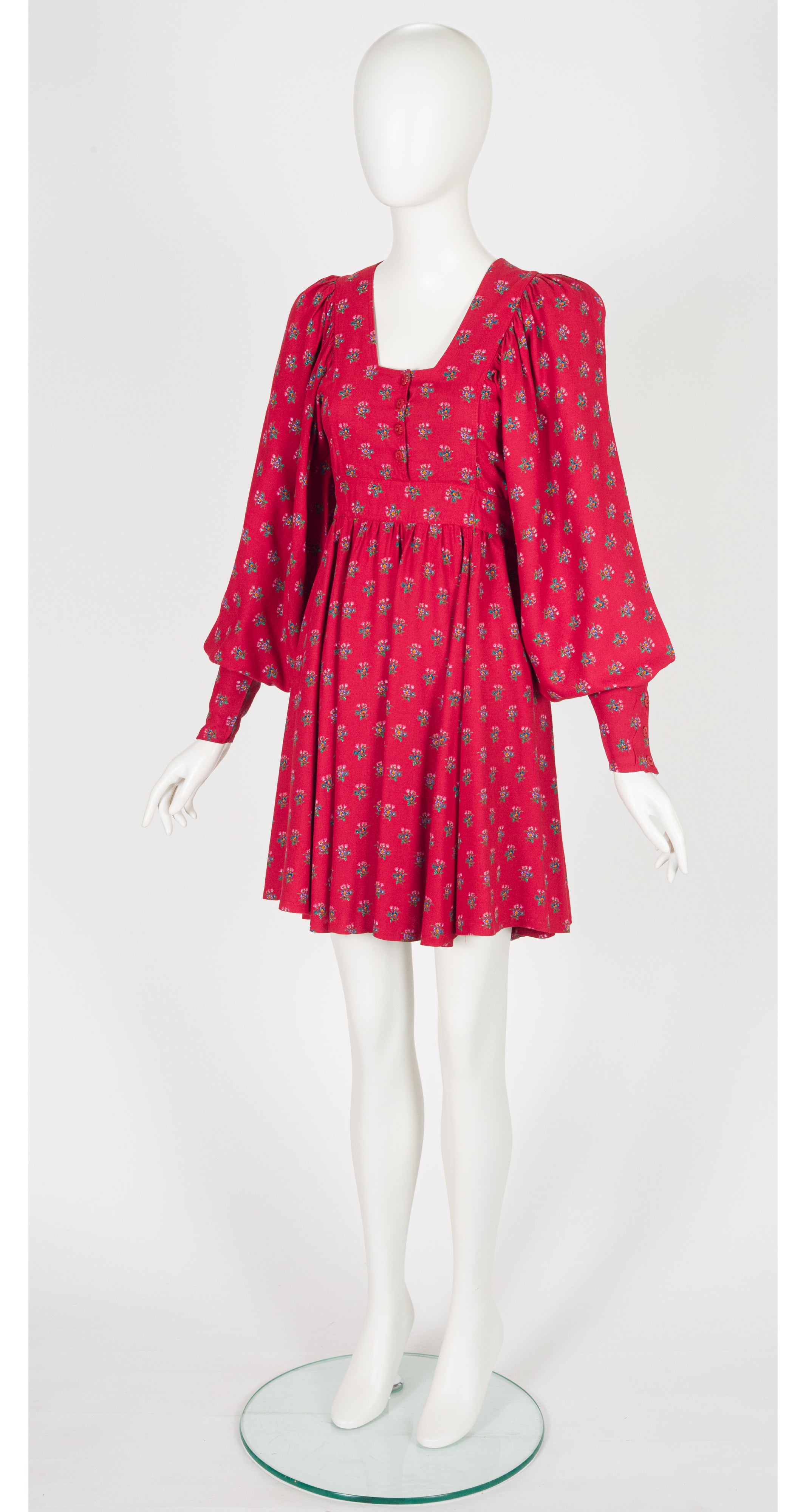 A 1970s Jeff Banks red and pink patterned mini dress with voluminous puff sleeves and a square neckline, displayed on a white mannequin against a light gray background.