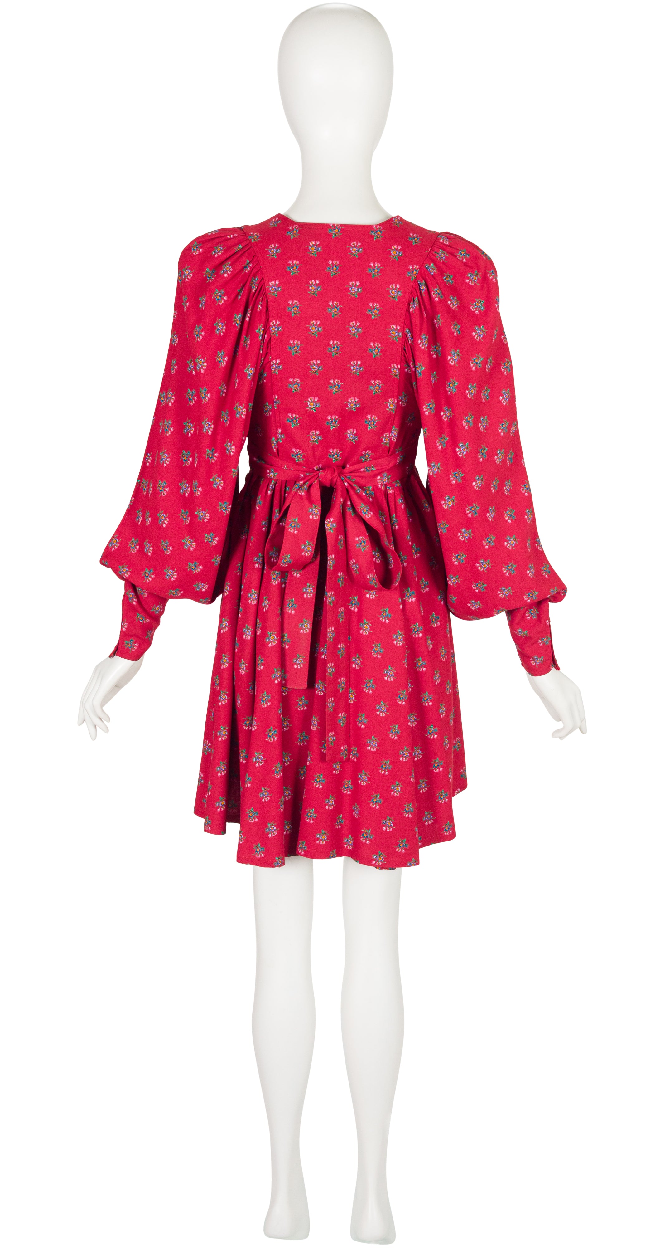A 1970s Jeff Banks red and pink patterned dress displayed on a white mannequin against a plain white background. The dress features puff sleeves, a self-tie waist belt, and a small repeating floral print.